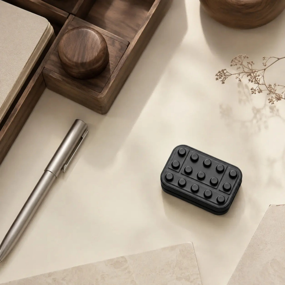 Overhead view of the Brix fidget slider on a desk beside a pen, wooden tray, and dried branch.