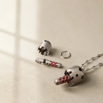 Daze pendant on a chain beside a separate bell shell, connecting rods, and ring on a pale surface.