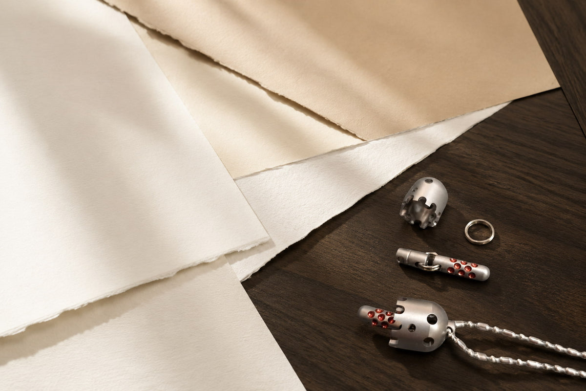 Daze pendant and separate components arranged on a dark wooden surface beside pale sheets of paper.