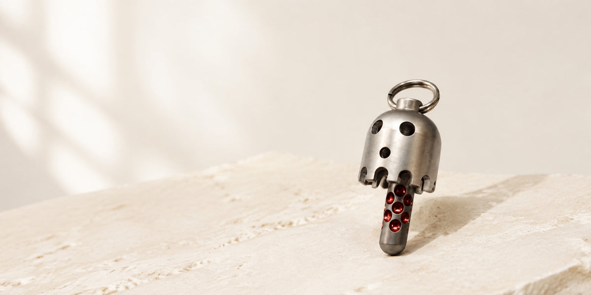Daze bell pendant standing on a pale textured surface, showing its cutout face and red connecting rod.