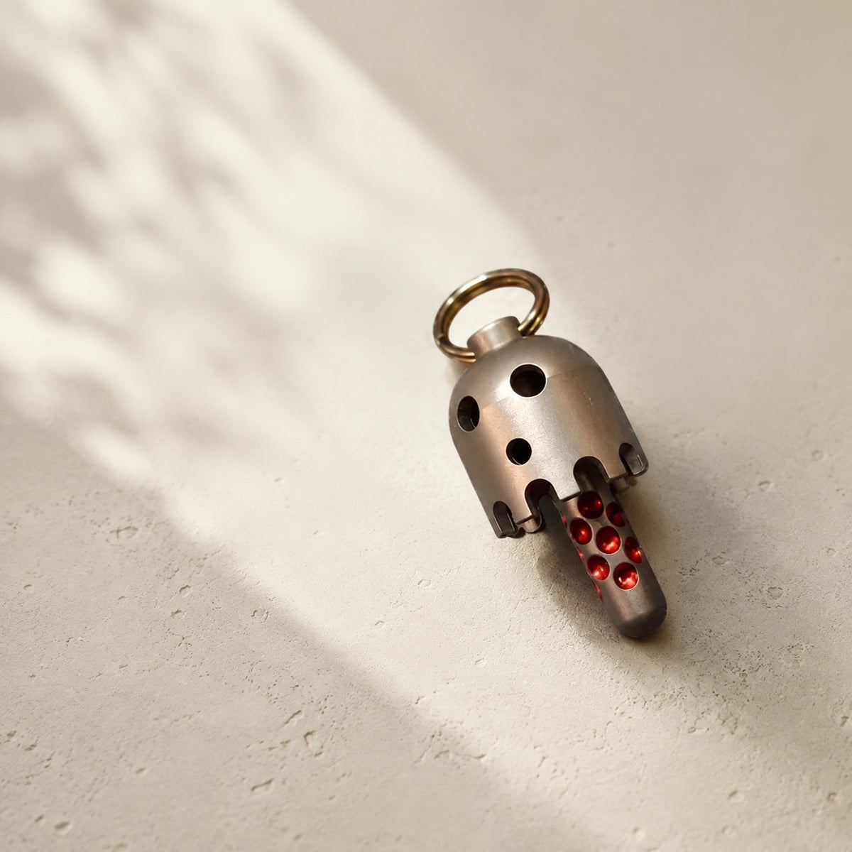 Daze bell pendant resting on a pale surface, with its round face cutouts and red details visible.