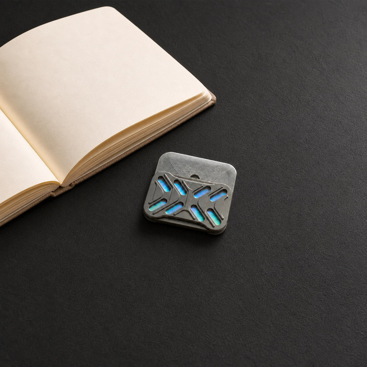 Gleam desk fidget slider with offset plates beside an open notebook on a dark surface.