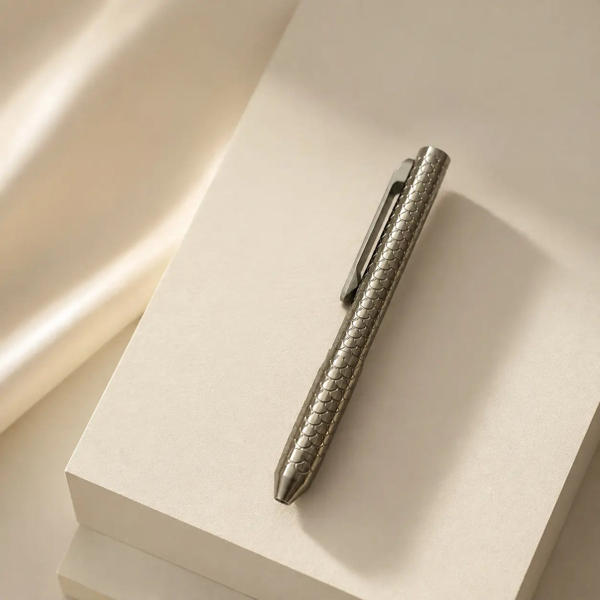 Imbra pen resting diagonally on a pale rectangular block beside folded fabric