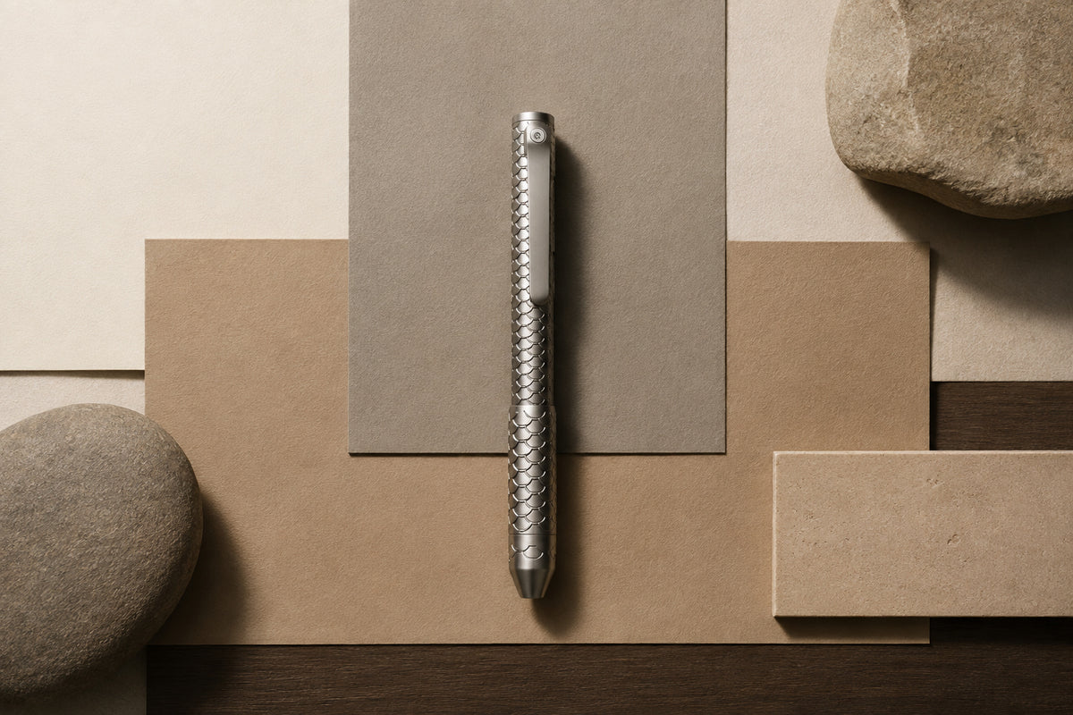Imbra pen arranged vertically on layered neutral-colored paper with stones nearby