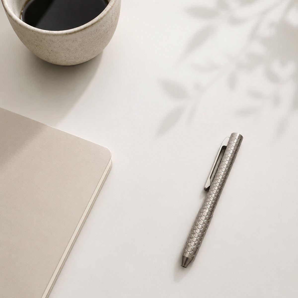 Imbra pen beside a notebook and a cup on a sunlit desk