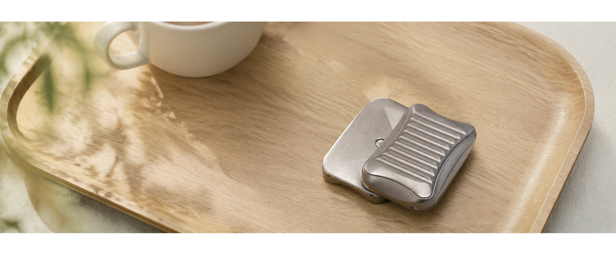 Stria magnetic slider resting on a wooden tray beside a cup and green leaves.