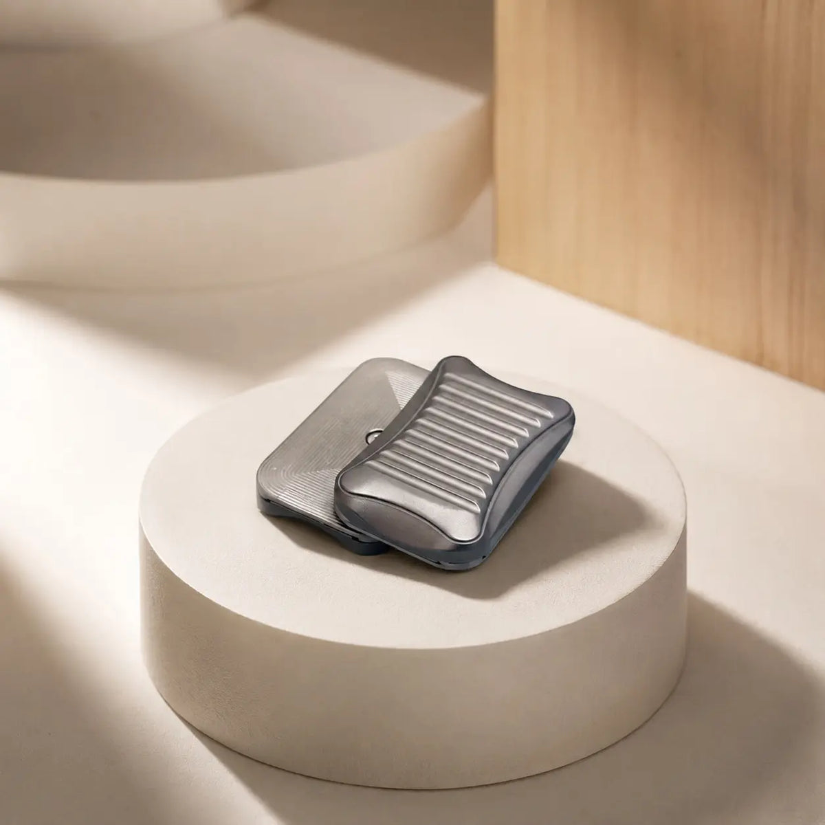 Stria magnetic slider with rounded corners and offset plates on a pale circular stand.