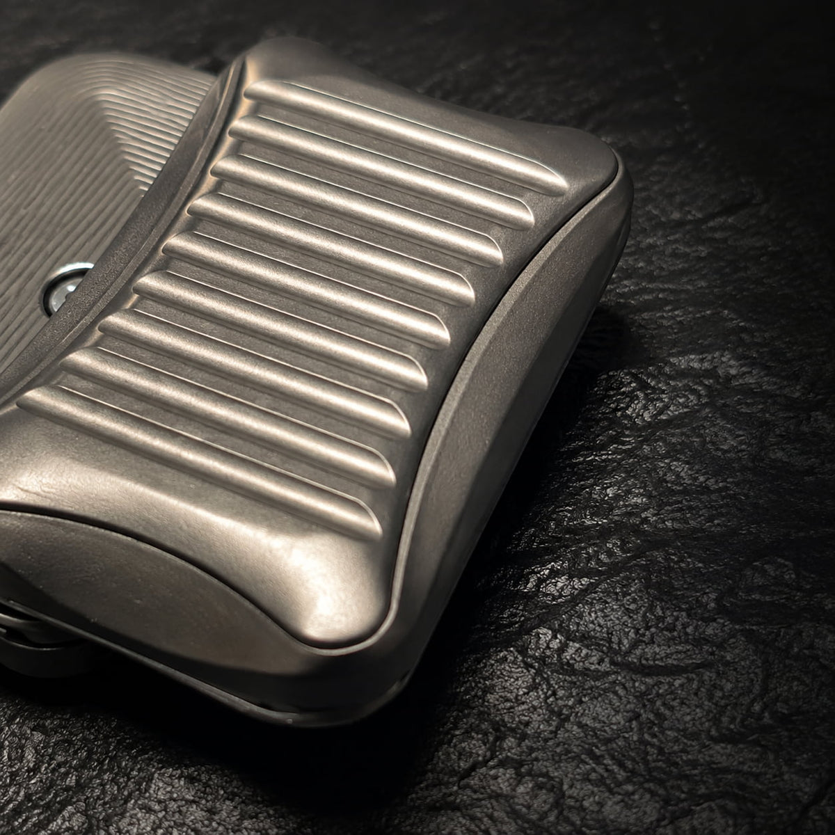 Close-up of the grooved face and curved front edge of the Stria fidget slider on a dark textured surface.